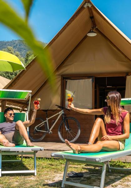 Two people toasting outside a tent in the mountains.