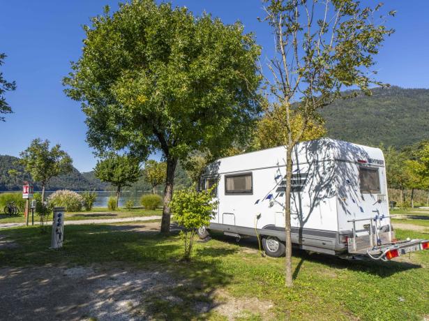 Camper parked by a lake, surrounded by trees.