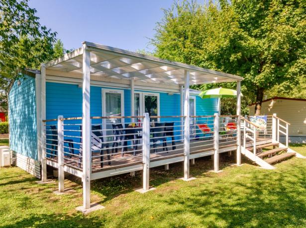 Blue mobile home with veranda and chairs on green lawn.