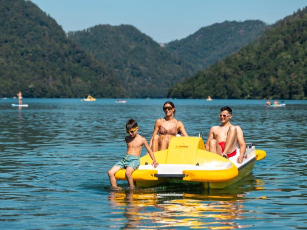 Family on a yellow pedal boat in a mountain-surrounded lake.