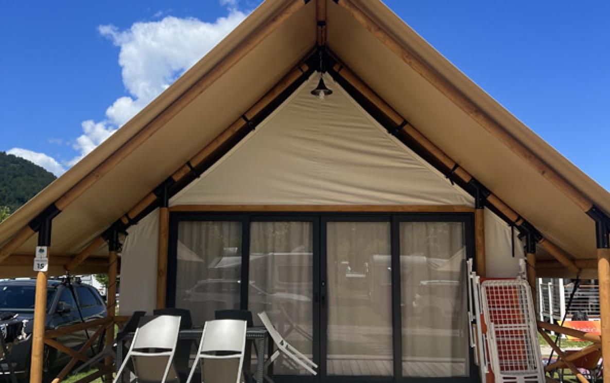 Modern glamping tent with wooden deck and chairs.