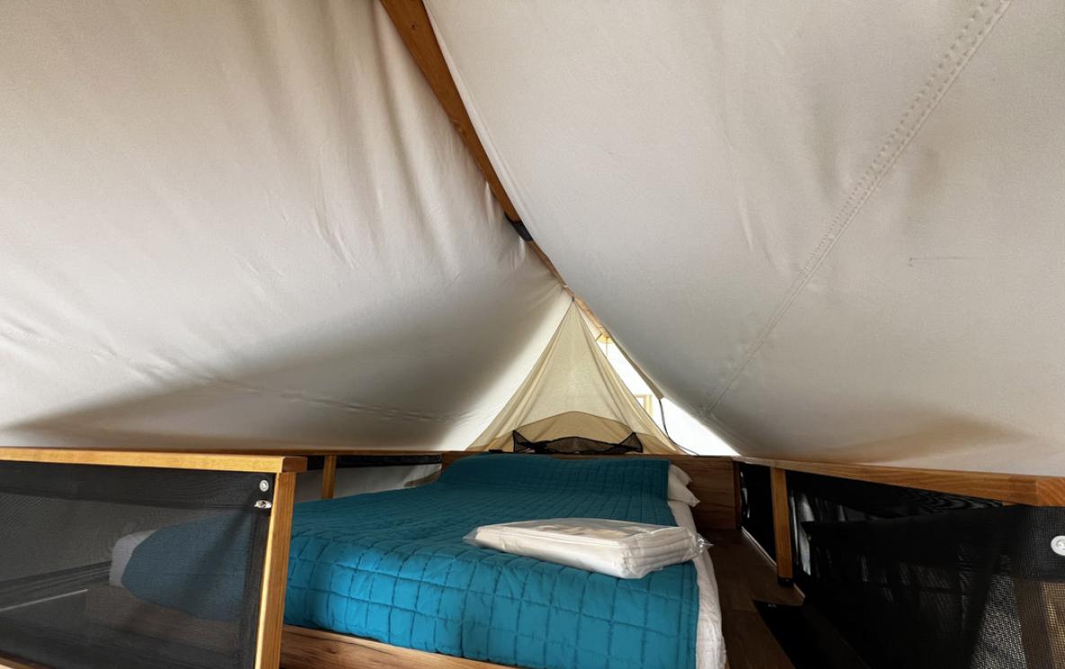 Inside a tent with a double bed and blue blanket.