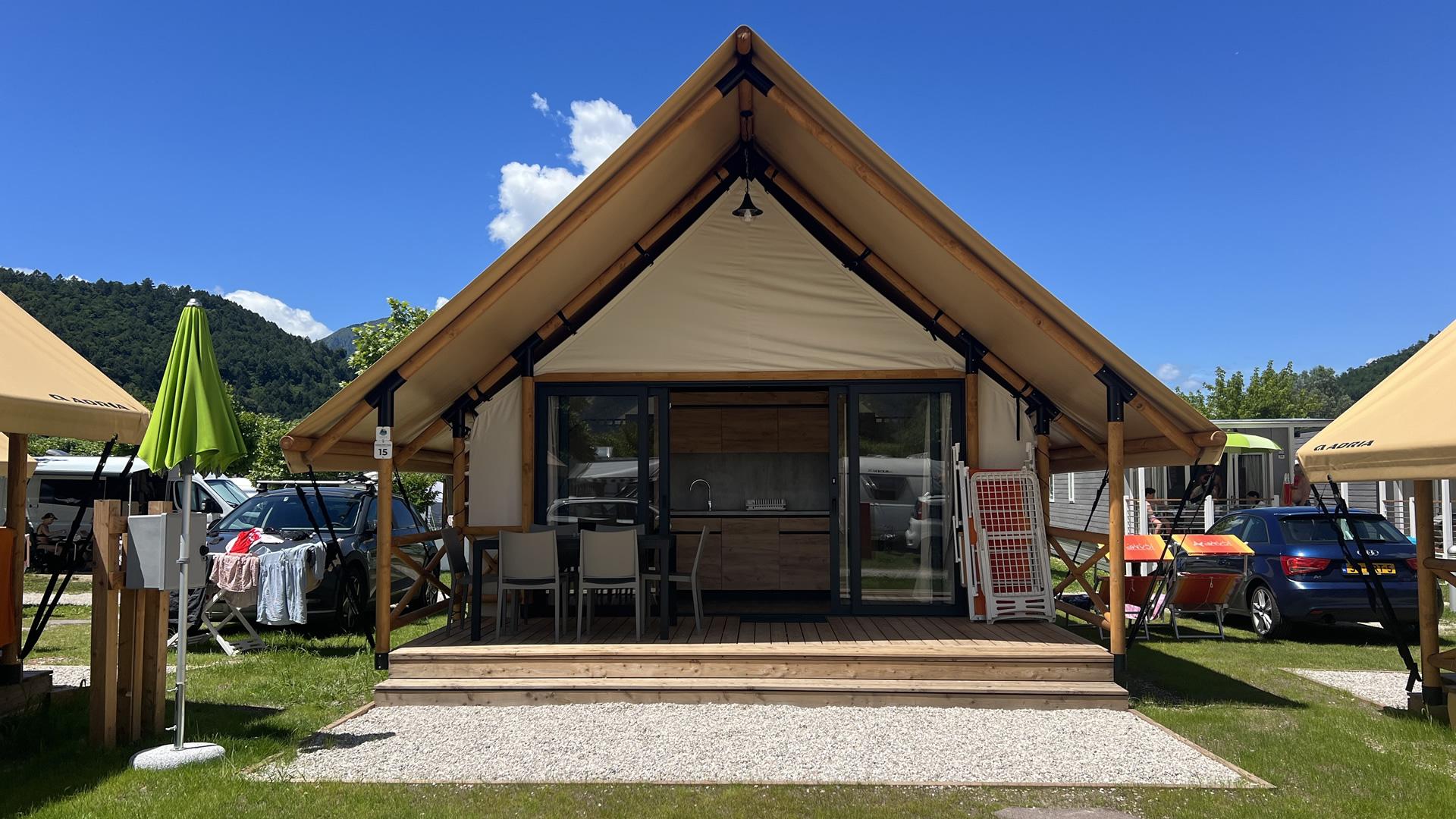 Glamping tent with porch in campsite, car and mountains in background.