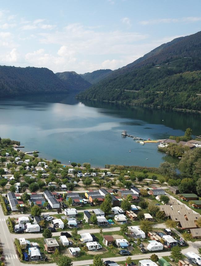 Panorama di un lago con campeggio e montagne sullo sfondo.