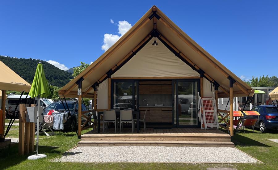 Tenda glamping con veranda in campeggio, auto e montagne sullo sfondo.